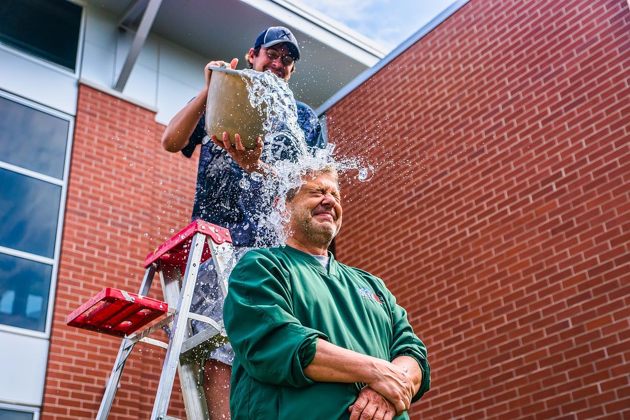 Image of a person in green being dumped with a bucket of ice water